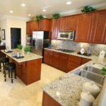A totally remodeled kitchen with a new island, chairs cabinetry, sink, and appliances.